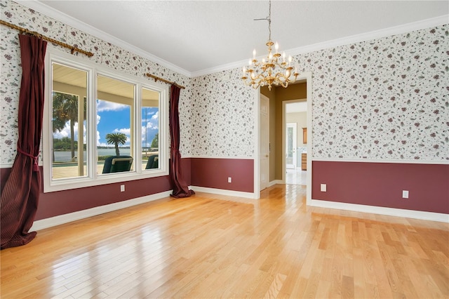 spare room featuring a notable chandelier, baseboards, light wood-type flooring, wallpapered walls, and crown molding