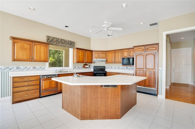 kitchen with under cabinet range hood, light countertops, an island with sink, and black appliances