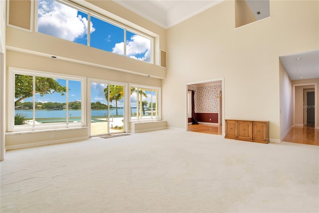 unfurnished living room featuring a high ceiling, a water view, baseboards, ornamental molding, and carpet