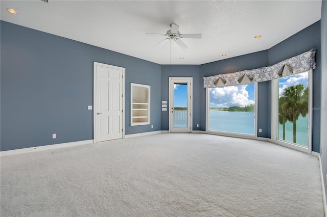 empty room with baseboards, a ceiling fan, light colored carpet, a water view, and recessed lighting