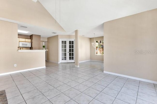 unfurnished room with high vaulted ceiling, light tile patterned flooring, a notable chandelier, baseboards, and french doors