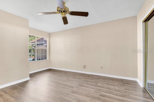 empty room with ceiling fan, a textured ceiling, baseboards, and wood finished floors