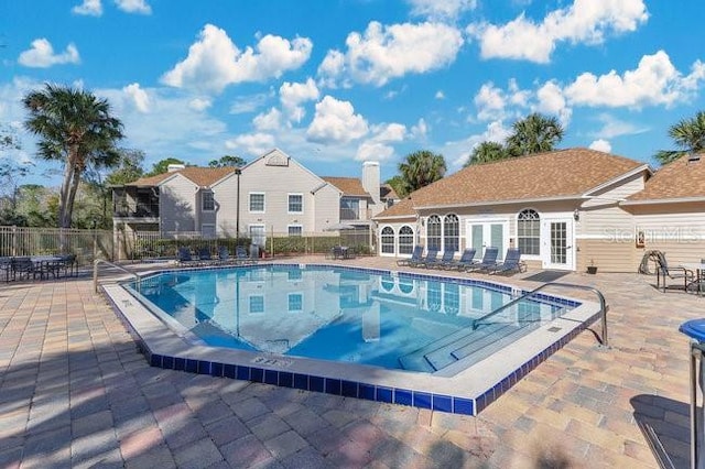 community pool with a patio area, fence, and an outbuilding