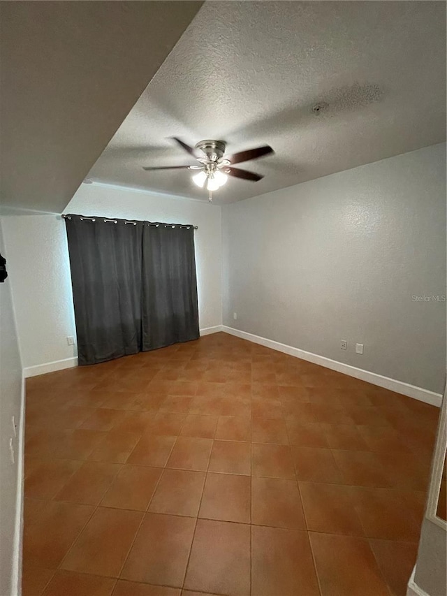 tiled empty room featuring ceiling fan and a textured ceiling