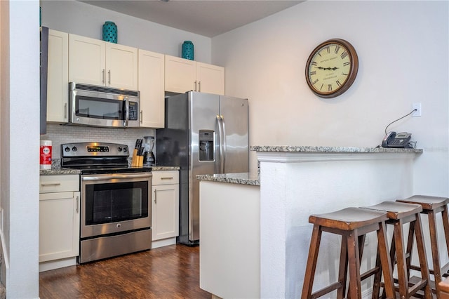 kitchen with appliances with stainless steel finishes, light stone countertops, a breakfast bar area, and white cabinets