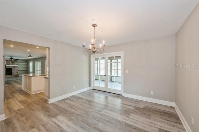 interior space featuring french doors, light wood-style floors, a brick fireplace, baseboards, and ceiling fan with notable chandelier