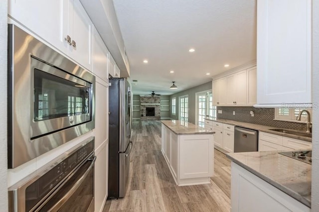 kitchen featuring light stone counters, stainless steel appliances, decorative backsplash, a large fireplace, and a sink