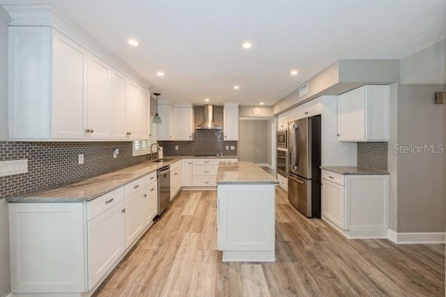 kitchen with stainless steel appliances, a sink, white cabinets, a center island, and wall chimney exhaust hood