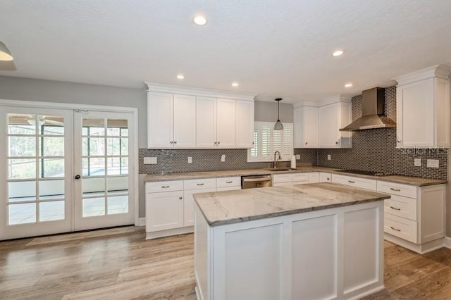 kitchen with french doors, stainless steel dishwasher, white cabinets, a sink, and wall chimney exhaust hood