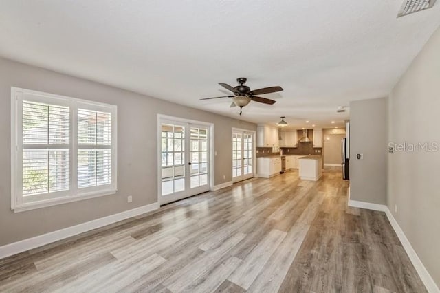 unfurnished living room featuring light wood-type flooring, a healthy amount of sunlight, and baseboards