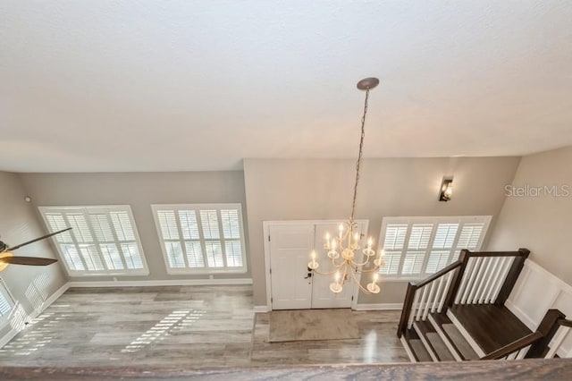 entryway with ceiling fan with notable chandelier, wood finished floors, and baseboards