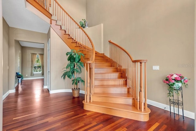 staircase with wood finished floors, baseboards, and a towering ceiling