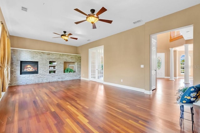 unfurnished living room with visible vents, wood finished floors, a fireplace, and ornate columns