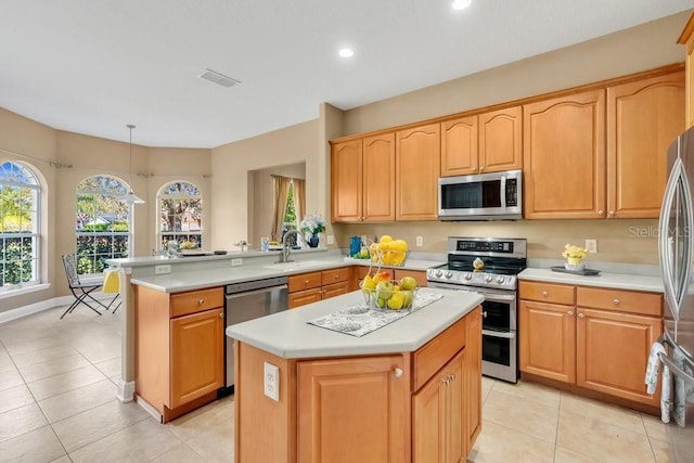 kitchen with a peninsula, a sink, light countertops, appliances with stainless steel finishes, and a center island