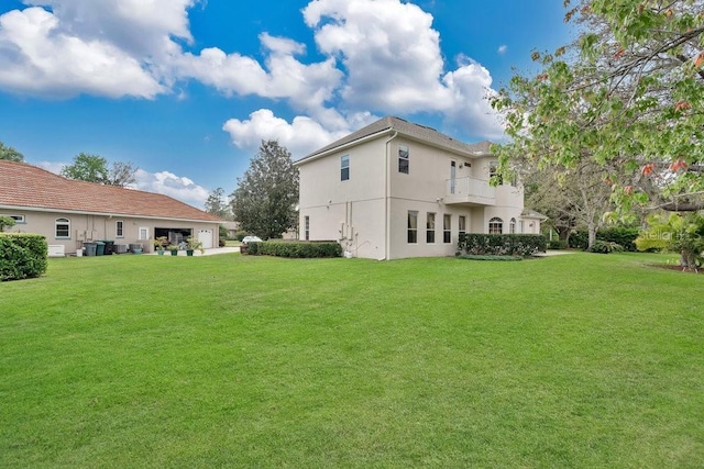 back of property featuring a balcony, a yard, and stucco siding