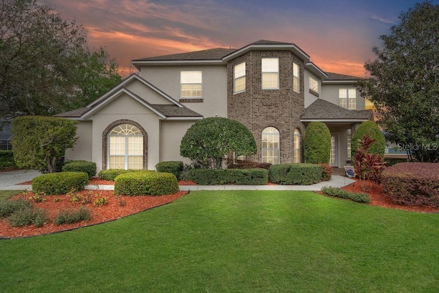 view of front of home with brick siding, stucco siding, and a lawn