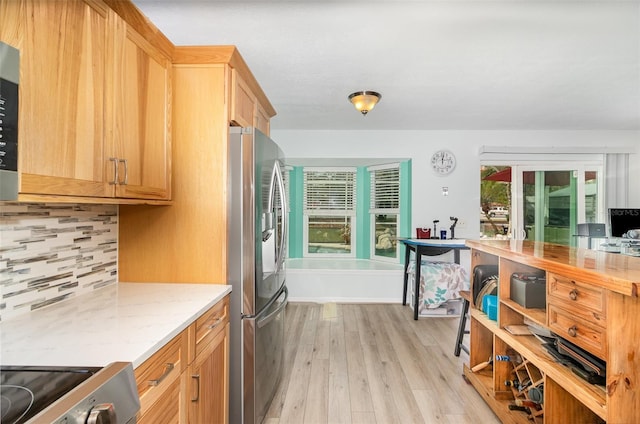 kitchen with light stone countertops, light wood-type flooring, stainless steel refrigerator with ice dispenser, backsplash, and range