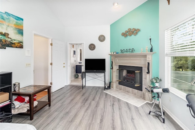 living area featuring lofted ceiling, light wood-style flooring, baseboards, and a tiled fireplace