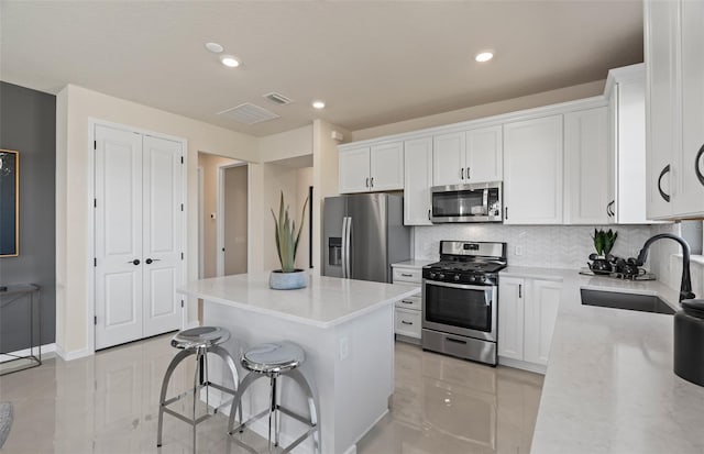 kitchen with sink, white cabinetry, a center island, appliances with stainless steel finishes, and decorative backsplash