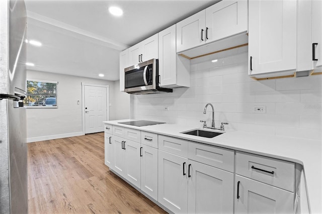 kitchen with white cabinets, stainless steel microwave, black electric stovetop, light countertops, and a sink