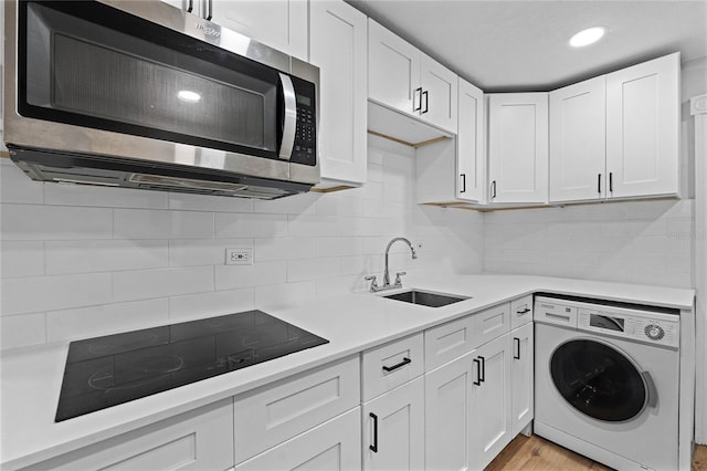 kitchen featuring light countertops, stainless steel microwave, white cabinets, washer / dryer, and black electric cooktop