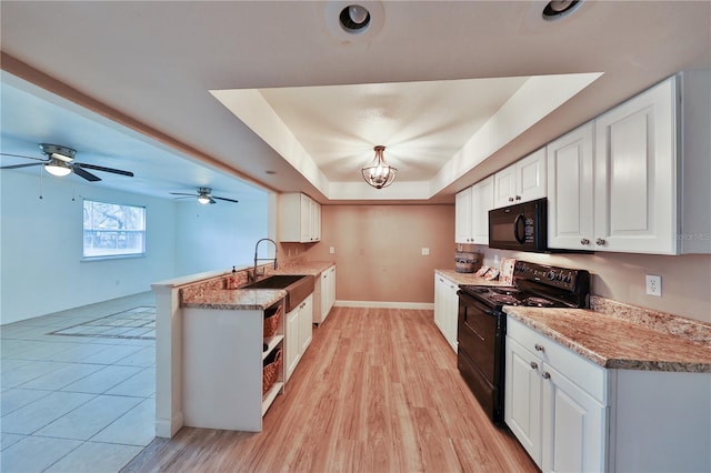 kitchen with black appliances, white cabinetry, sink, a tray ceiling, and light hardwood / wood-style flooring