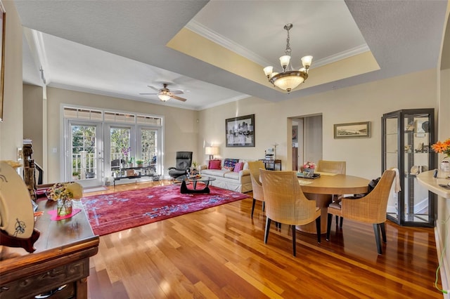 dining area featuring hardwood / wood-style flooring, french doors, a raised ceiling, ceiling fan with notable chandelier, and ornamental molding