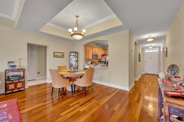 dining space with a raised ceiling, an inviting chandelier, light hardwood / wood-style flooring, and ornamental molding