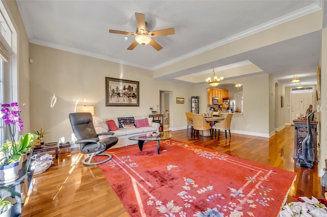 living room featuring hardwood / wood-style floors, a raised ceiling, ceiling fan with notable chandelier, and ornamental molding