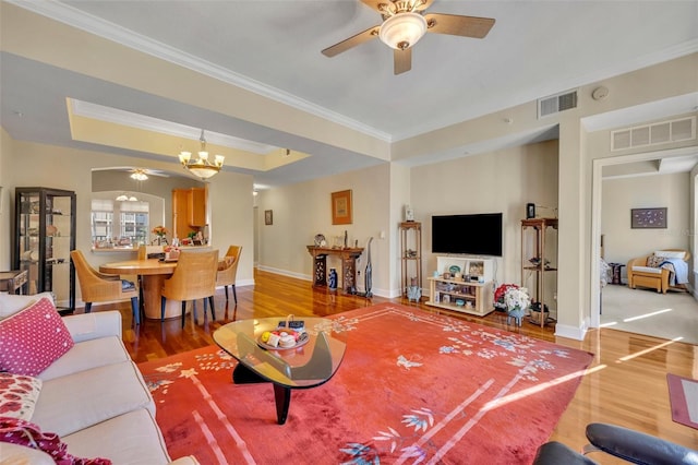 living room featuring ceiling fan with notable chandelier, crown molding, hardwood / wood-style flooring, and a tray ceiling