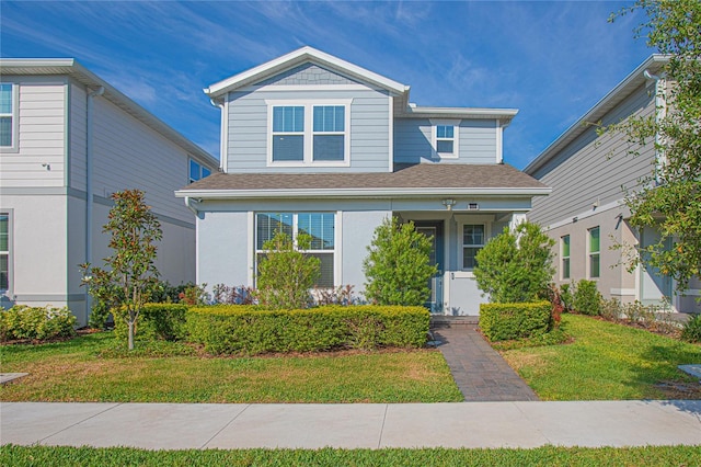 view of front of house featuring a front lawn, a shingled roof, and stucco siding