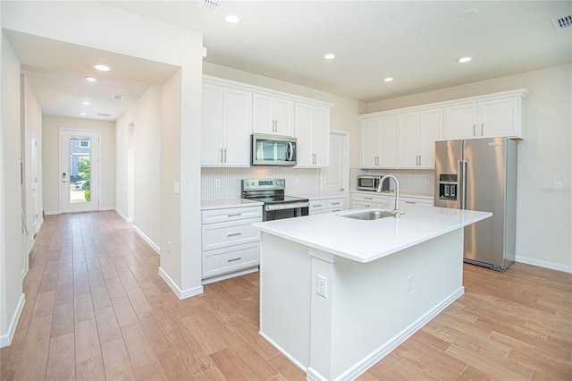 kitchen with light wood finished floors, tasteful backsplash, white cabinets, appliances with stainless steel finishes, and a sink