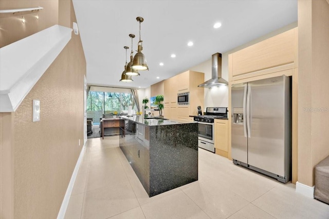 kitchen with a center island with sink, hanging light fixtures, appliances with stainless steel finishes, light brown cabinets, and wall chimney range hood