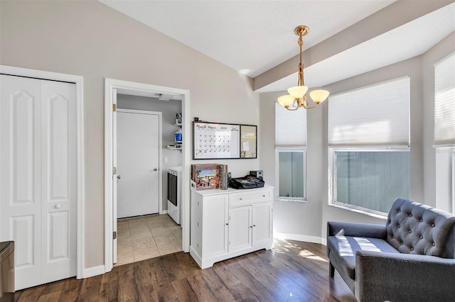 living area with baseboards, dark wood finished floors, lofted ceiling, a chandelier, and separate washer and dryer