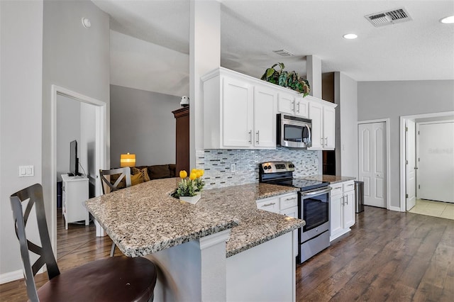 kitchen featuring visible vents, lofted ceiling, a peninsula, stainless steel appliances, and white cabinetry