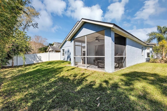 rear view of house featuring a sunroom, a ceiling fan, fence, and a lawn