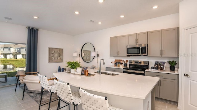 kitchen with gray cabinetry, sink, stainless steel appliances, and a center island with sink