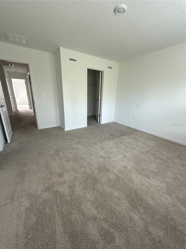 unfurnished bedroom with baseboards, visible vents, a walk in closet, a textured ceiling, and carpet floors