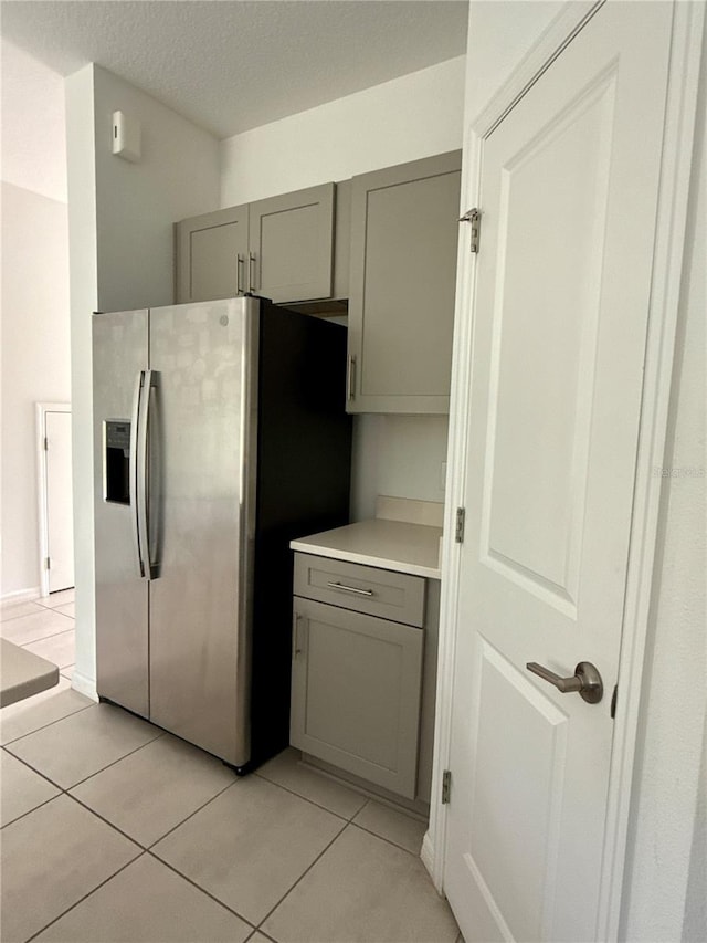 kitchen featuring light tile patterned floors, a textured ceiling, light countertops, stainless steel refrigerator with ice dispenser, and gray cabinets