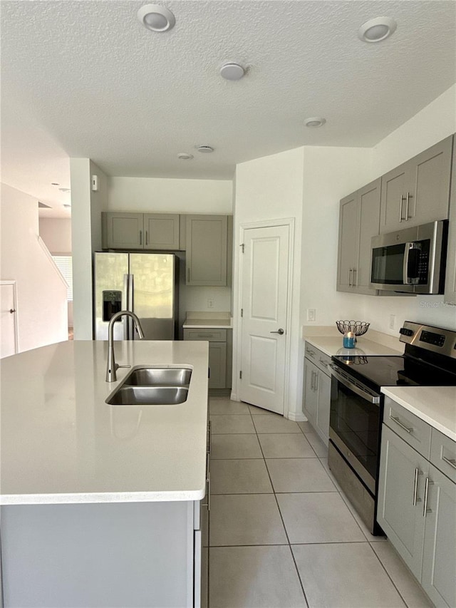 kitchen with light tile patterned floors, a center island with sink, appliances with stainless steel finishes, light countertops, and a sink