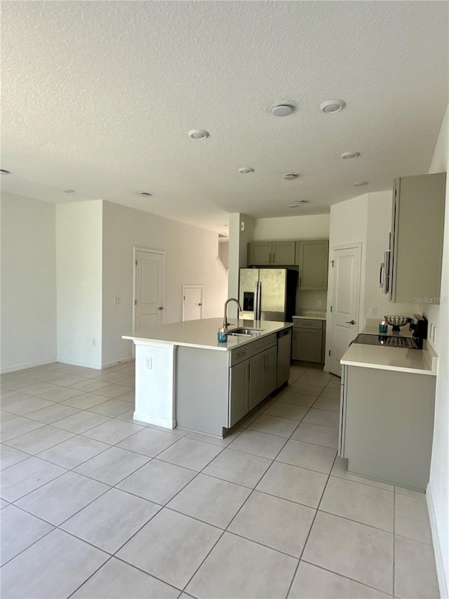 kitchen with light countertops, an island with sink, stainless steel refrigerator with ice dispenser, and gray cabinets