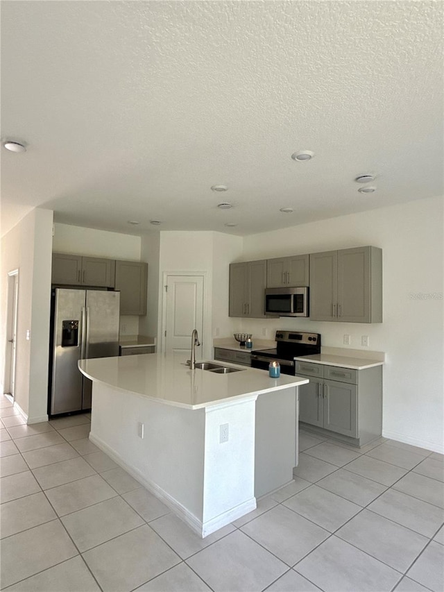 kitchen featuring an island with sink, appliances with stainless steel finishes, light countertops, gray cabinetry, and a sink