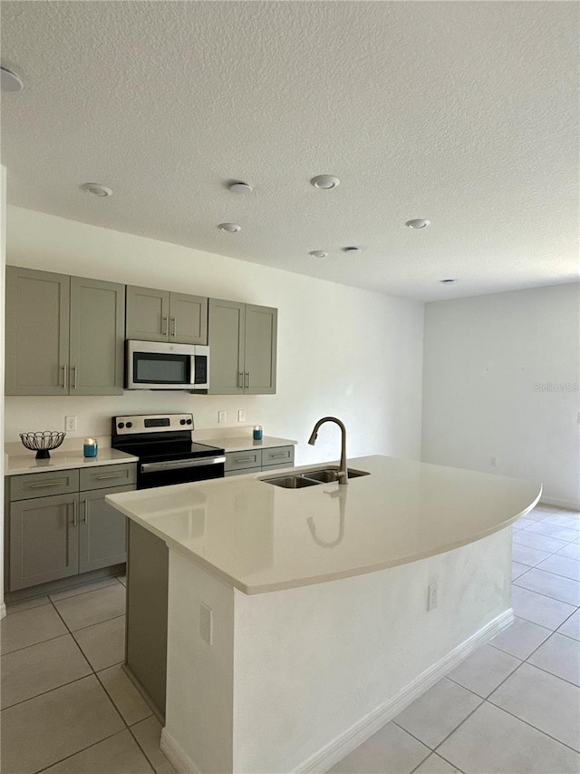 kitchen with light countertops, appliances with stainless steel finishes, an island with sink, and a sink