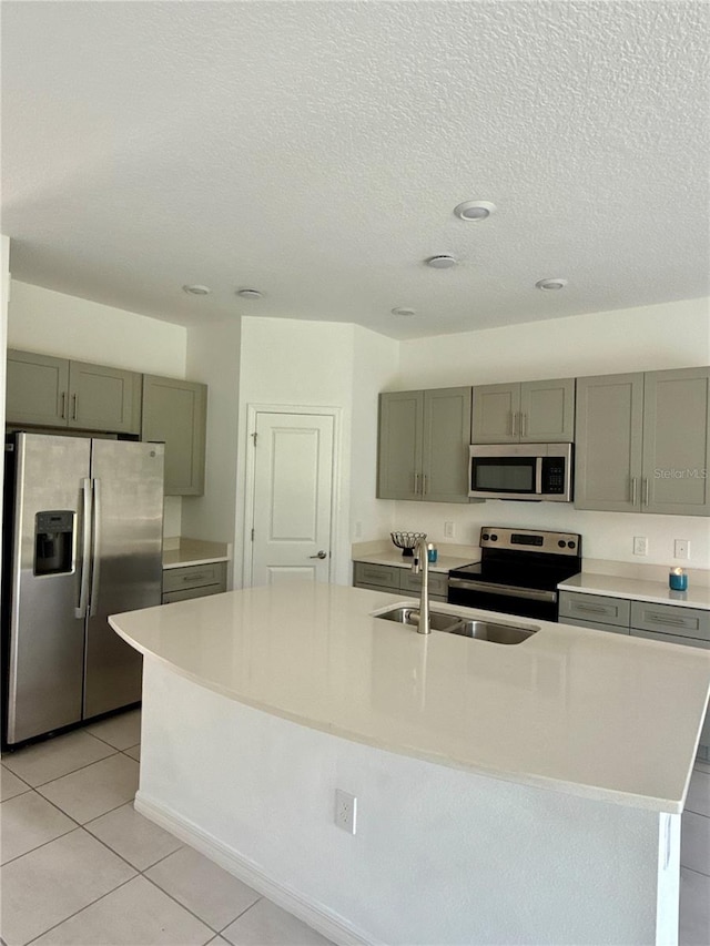 kitchen featuring light tile patterned floors, a kitchen island with sink, stainless steel appliances, light countertops, and a textured ceiling