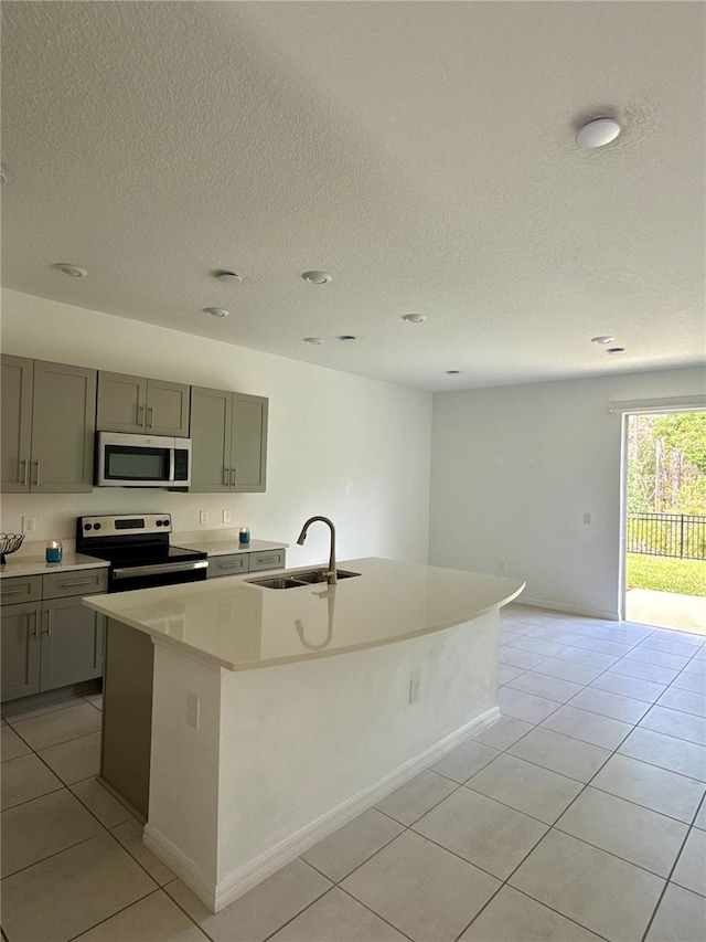 kitchen with light tile patterned floors, an island with sink, appliances with stainless steel finishes, light countertops, and a sink