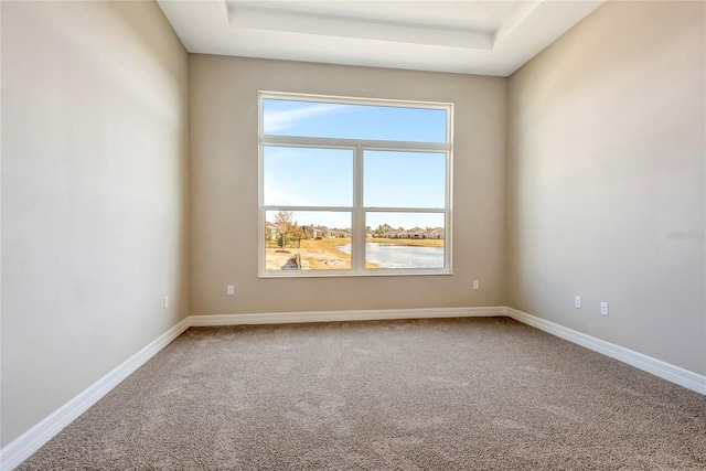 carpeted empty room featuring a water view and a tray ceiling