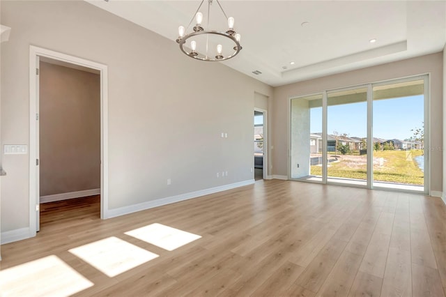 spare room featuring a tray ceiling, light hardwood / wood-style floors, and a chandelier