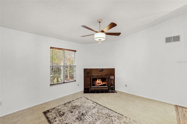 living area with a textured ceiling, visible vents, a tiled fireplace, and carpet flooring