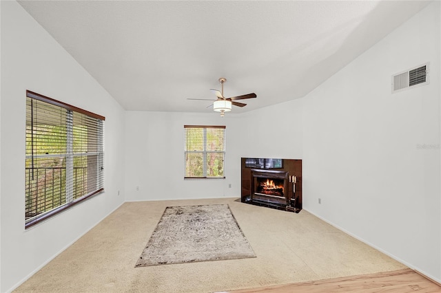 living room featuring carpet floors, lofted ceiling, visible vents, a fireplace with flush hearth, and ceiling fan