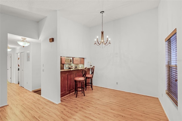 dining area with a chandelier, light wood-type flooring, baseboards, and a high ceiling